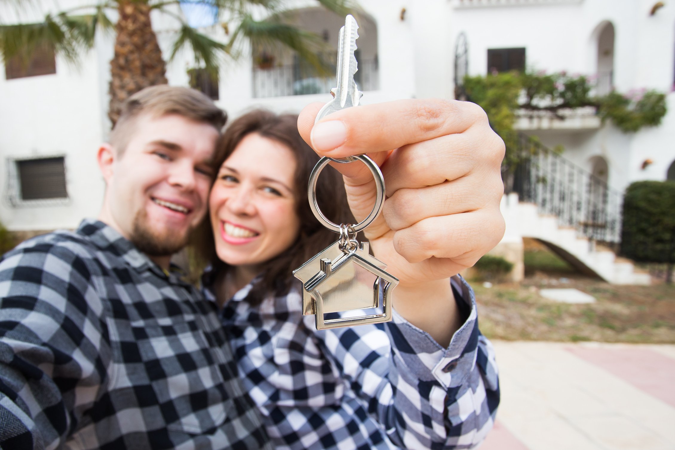 Moving and Real Estate Concept - Happy Young Laughing Cheerful Couple Man and Woman Holding Their New Home Keys in Front of a House.